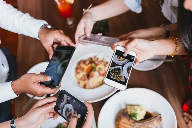 Existing customers taking a photo of the different dishes served on their table to post on a social media platform.