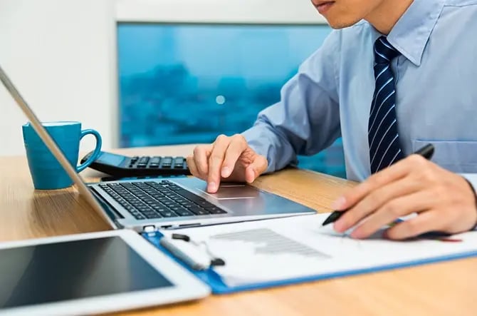 Photo of an insurance agent working on a laptop while writing on a clipboard.