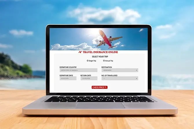 Travel insurance website on a laptop screen on a wooden desk with a blurry summer beach in the background.