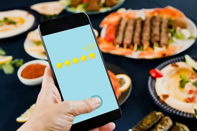 Close up of a hand using a smartphone to give 5 stars about restaurant food and service.