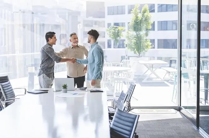 Three businessmen are shaking hands around a conference table.