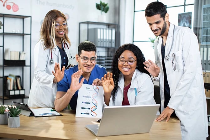 Four multiracial doctors in uniforms waving to a laptop during video online conference.