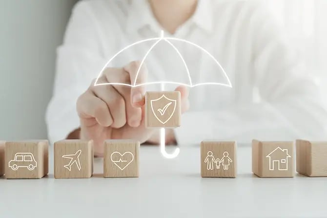 Photo of a hand holding a security icon on a wooden cube for life insurance concept. Other cubes indicate home insurance, travel insurance, health insurance, family insurance, and home insurance.