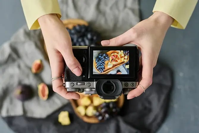 High angle view of photographer taking a photo of fresh fruits on wooden board using a professional camera.