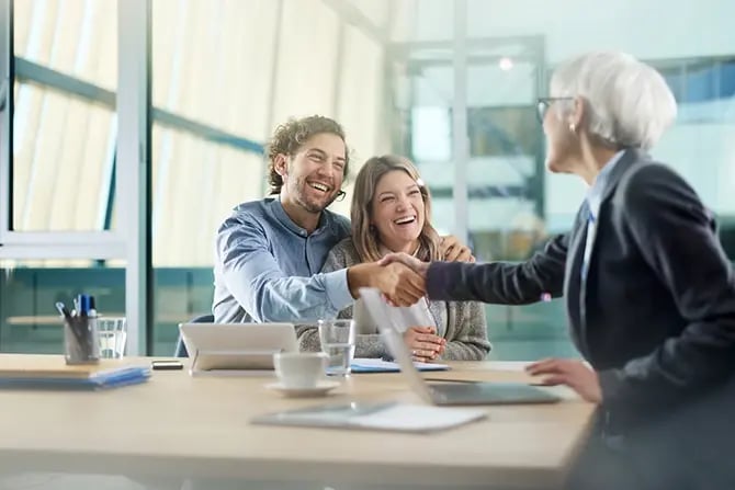 Young happy couple shaking the hand of their insurance agent during a meeting in the office.