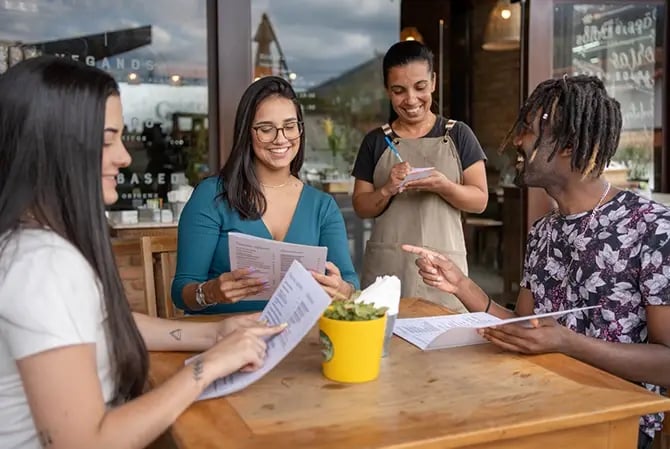 Group of friends giving a server their order while sitting at a table together outside at a sidewalk cafe.