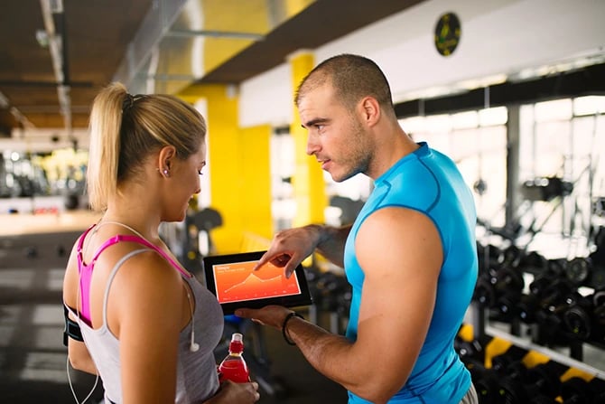 Sporty woman is discussing workout progress and statistics with her fitness instructor using a digital tablet.