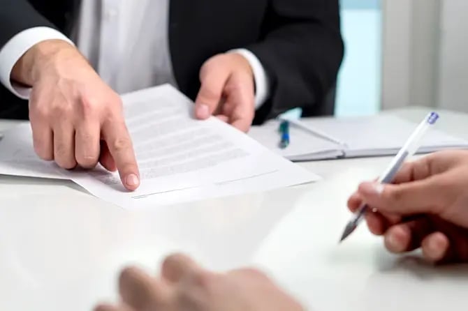 Close up image of contract signing. Insurance agent pointing to the line for signature in a document paper.