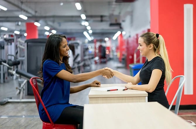 Happy woman signs up for the gym and shakes the hand of the customer service representative in a local business.